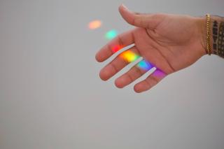 An outstretched hand, palm facing the camera, with a rainbow of light cast on it by a prism.