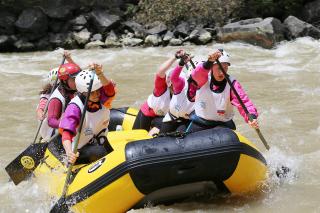 crew of rafters working together to get a yellow raft through the rapids on a river