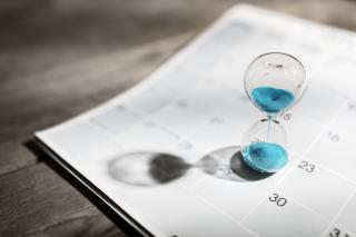 A clear hourglass filled with blue sand rests on the page of a calendar 