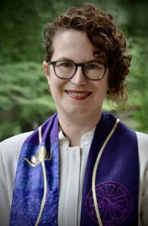 Amanda Poppei smiles outdoors, wearing an ivory clergy robe and purple stole.