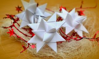 On a nest of straw and holiday tinsel three white paper stars, or Froebelsterne, are nestled. 