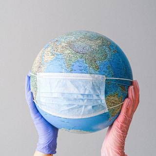 Gloved hands hold up a globe wearing a surgical face mask
