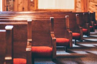 In a sunny church sanctuary, rows of empty red velvet and wooden pews 