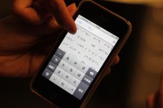 A hand, holding an older model iPhone, with a menu in Japanese for many different emoticons.