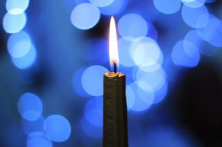 A lit taper candle burns against a blurred background of blue holiday lights.