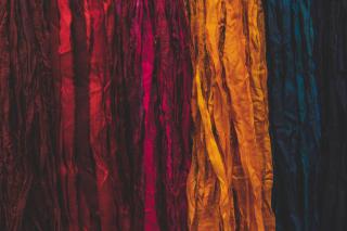 Strips of fabric in bold colors -- magenta, saffron, indigo -- hang vertically. 