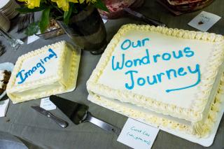 2 cakes, one each with and without nuts & gluten. Decorated with words "Imagine" and "Our Wondrous Journey"
