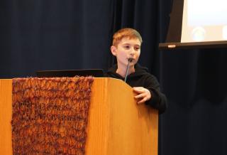 image of a young male speaking a podium with a  microphone