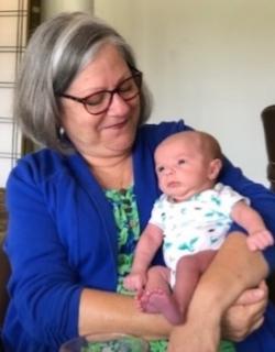 Denise Rimes, wearing a green blouse and blue sweater, holds her baby grandchild in her lap