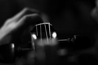 Cellist playing cello during concert, in a black and white close up that makes the neck of the cello appear somewhat abstract.