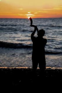 Man in silhouette playing a shofar during sunset on Lake Erie 