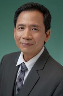 Headshot of Jonipher Kwong wearing a gray suit with dark green background.