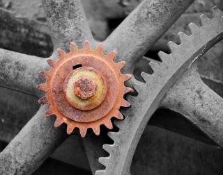 A small rusted gear on a wheel hub with teeth engaged with a much larger gray gear