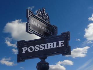 intersecting street signs, with the words "impossible" and "possible," in front of blue sky and clouds background