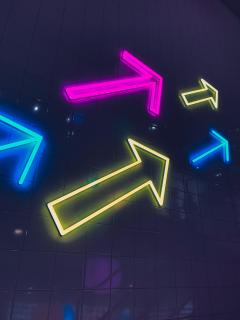 Against a dark field, five neon arrows in blue, pink, and yellow point in the same direction.