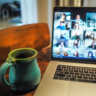 Teal coffee cup sitting next to an open laptop with lots of people's images on it, as though in an online class.. Photo by Chris Montgomery on Unsplash.