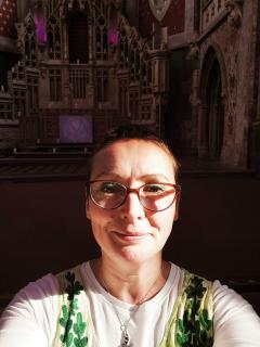Laura Dobson, wearing glasses, is shown in a beam of sunlight in front of a cathedral's chancel