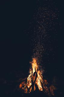 A bonfire sends sparks flying upwards, against a pitch black background.