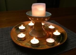 A chalice and a circle of votive candles on a ceramic plate with a spiral pattern.