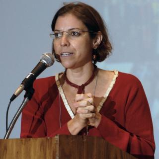 Maria Rodriguez, hands clasped, speaking into a microphone.