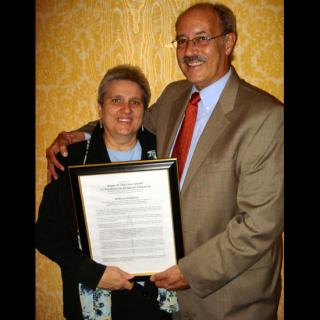 William Sinkford (right) stands with his arm around Judith Frediani's shoulders; together, they hold and display the 2009 Angus MacLean Award.