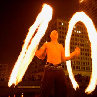 A bare chested performer spins circles of fire with both arms.