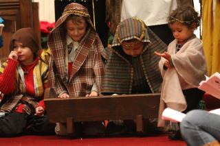 Small children, in costume, lean over a manger during a church Christmas pageant