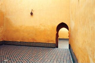 Against a stark gold wall, with ornate floor tiles, a curving doorway leads into the next room.