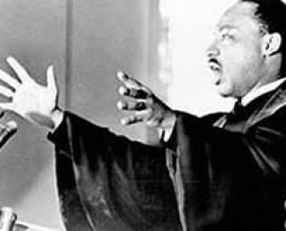 Dr. Martin Luther King, Jr. with his arms spread, speaking.