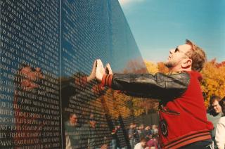 At the Vietnam Memorial Wall in Washington, a man places both hands on the wall and looks up to read names