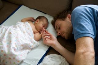 Sleeping baby and napping dad hold hands