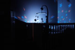 In a dark room, a lighted mobile over a baby's crib throws colored stars of light onto the walls.