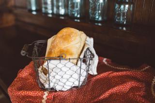 A metal basket, on a piece of cloth, holds a loaf of bread.