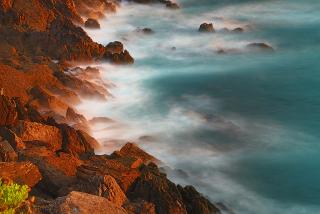 Foamy waves wash up on craggy rocks, made red by the sun, in Morrazo, Galicia (Spain)