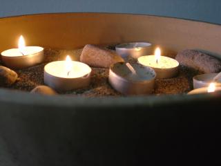 Several tea lights burn in a bowl of sand