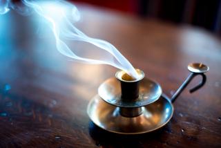 An empty brass candle holder emits a stream of smoke, suggesting that a candle has entirely burned itself out.