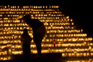 A wall of candles, with the silhouettes of a parent and child in front