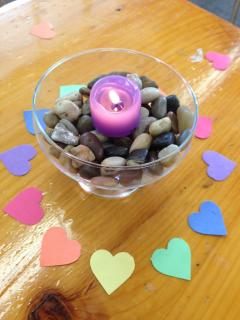Pink candle chalice surrounded by colorful paper hearts on wooden table.