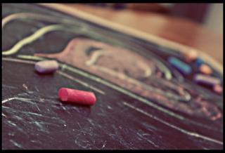 Two pieces of colored chalk, lying on a flat chalkboard, with a multi-colored heart drawn on it.