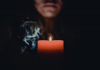 A red candle glows, and the bottom half of a person's face is visible.