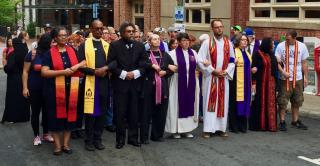 clergy wearing stoles walk arm in arm in the street