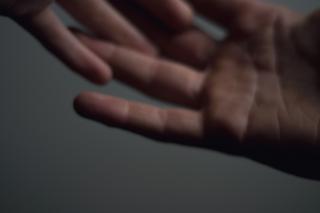 a pair of hands, only one entirely in the frame, with fingers loosely interlaced