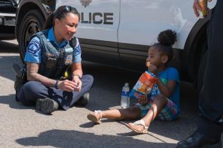 Smiling police officer sits on the ground talking to child