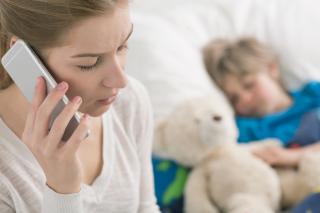 A woman speaks on a cell phone while, in the background, a child sleeps with a teddy bear