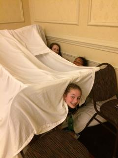 Three middle schoolers smile from their blanket fort