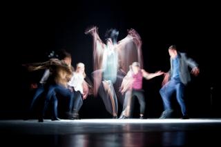 A group of dancers, lit from above, blurred by being caught in motion.