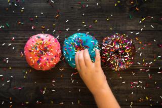 three donuts, with sprinkles, on a table. A child's hand is taking the center donut.