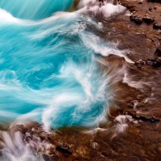 Ocean water swirls as it crashes against flat wet rocks.