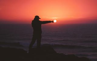 Against a brilliant sunset, a person in silhouette appears to punch the sun.