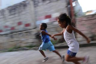 Two black children run, blurred, in joy and freedom down the street.